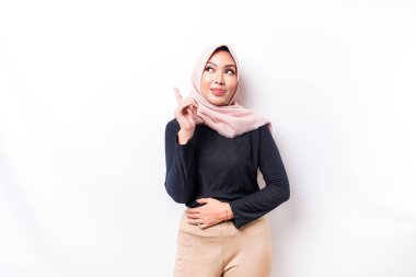 Starving Asian Muslim woman wearing a hijab, pointing up at the copy space above her, isolated by a white background