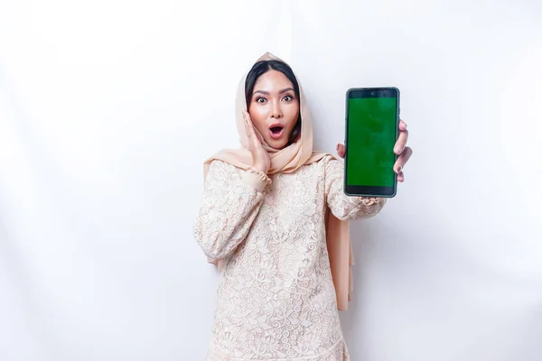 Shocked Asian woman wearing hijab, showing copy space on her phone screen, isolated by white background