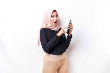 Shocked Asian woman wearing hijab, holding her phone, isolated by white background