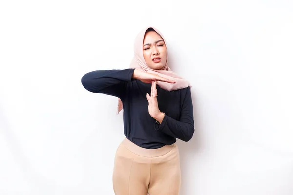 Disappointed Asian Muslim woman wearing a hijab gives thumbs down hand gesture of disapproval, isolated by white background
