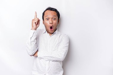 Shocked Asian man wearing white shirt pointing at the copy space on top of him, isolated by white background