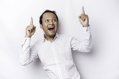 Excited Asian man wearing white shirt pointing at the copy space on top of him, isolated by white background