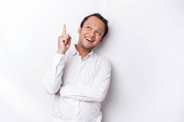 Excited Asian man wearing white shirt pointing at the copy space on top of him, isolated by white background