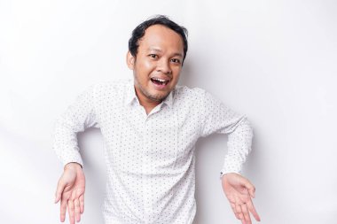Excited Asian man wearing white shirt pointing at the copy space below him, isolated by white background