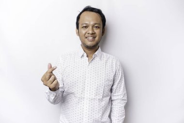 A happy young Asian man wearing a white shirt feels romantic shapes heart gesture expressing tender feelings