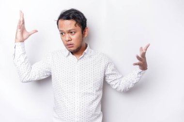 A portrait of an Asian man wearing a white shirt looks so confused between choices, isolated by a white background