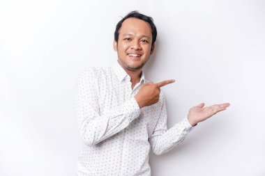 Excited Asian man wearing white shirt pointing at the copy space beside him, isolated by white background
