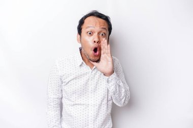 Young handsome man wearing a white shirt shouting and screaming loud with a hand on his mouth. communication concept.