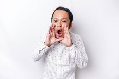 Young handsome man wearing a white shirt shouting and screaming loud with a hand on his mouth. communication concept.