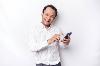 Excited Asian man wearing white shirt smiling while holding his phone, isolated by white background