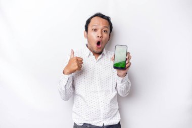Shocked Asian man wearing a white shirt and showing green screen on his phone, isolated by white background
