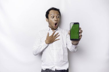 Shocked Asian man wearing a white shirt and showing green screen on his phone, isolated by white background