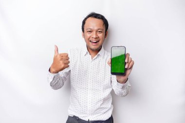 A portrait of a smiling Asian man wearing a white shirt and showing green screen on her phone, isolated by white background