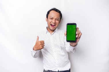 A portrait of a smiling Asian man wearing a white shirt and showing green screen on her phone, isolated by white background