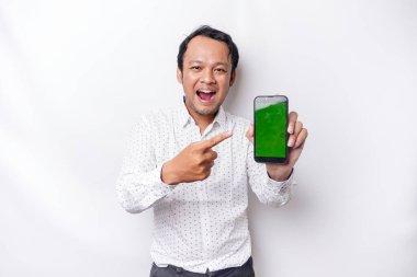 A portrait of a smiling Asian man wearing a white shirt and showing green screen on her phone, isolated by white background