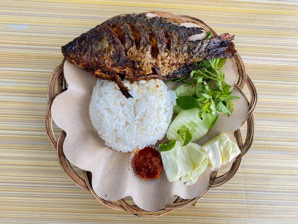a portrait of a grilled parrot fish with rice, veggies or lalapan, and chili sauce or sambal
