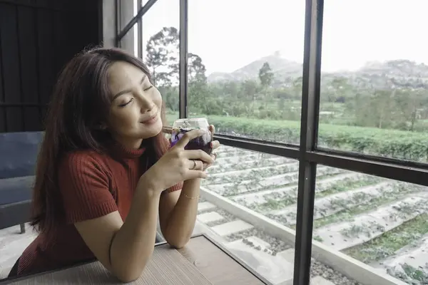 stock image Portrait of joyful young woman enjoying a cup of tea at home. Smiling pretty girl drinking telang tea in rainy season.