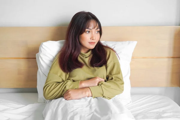 stock image Thoughtful Asian woman looks pensively above dressed in sweatshirt poses thinks about future while lying on the bed