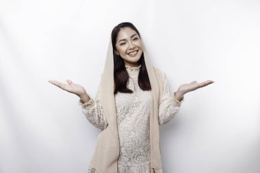 Young Asian Muslim woman smiling while pointing to copy space beside her