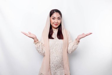 Young Asian Muslim woman smiling while pointing to copy space beside her