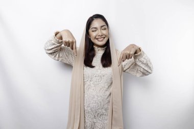 Excited Asian Muslim woman hijab pointing at the copy space below her, isolated by white background
