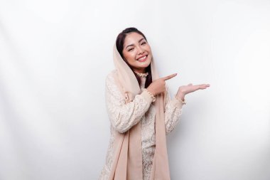 Young Asian Muslim woman smiling while pointing to copy space beside her