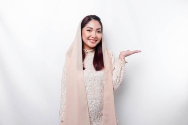Young Asian Muslim woman smiling while pointing to copy space beside her
