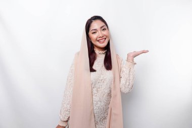 Young Asian Muslim woman smiling while pointing to copy space beside her