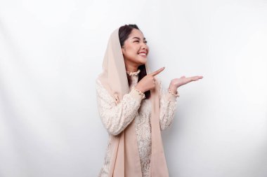 Young Asian Muslim woman smiling while pointing to copy space beside her