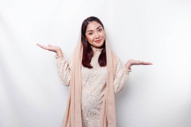 Young Asian Muslim woman smiling while pointing to copy space beside her