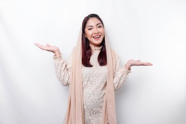 Young Asian Muslim woman smiling while pointing to copy space beside her