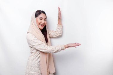 Young Asian Muslim woman smiling while pointing to copy space beside her