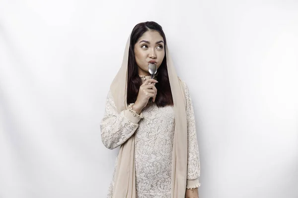 stock image An Asian Muslim woman is fasting and hungry and holding utensils cutlery while looking aside thinking about what to eat