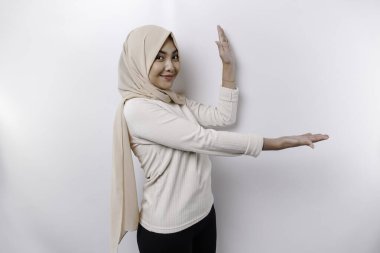 Young Asian Muslim woman smiling while pointing to copy space beside her