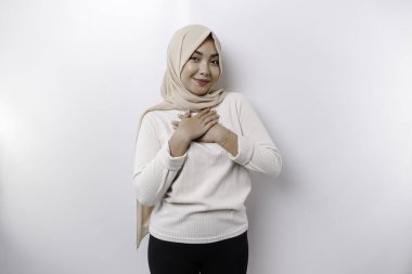 Happy mindful thankful young Asian Muslim woman with her hand on her chest smiling isolated on white background