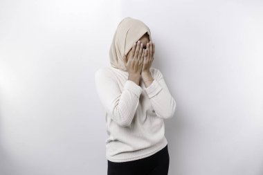 Young Asian Muslim woman isolated on white background, looks depressed, face covered by arms frightened and nervous.