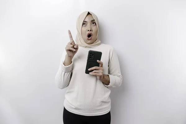 Zszokowana Azjatycka Muzułmanka Hidżabie Wskazująca Miejsce Ksero Trzymając Telefon Odizolowana — Zdjęcie stockowe