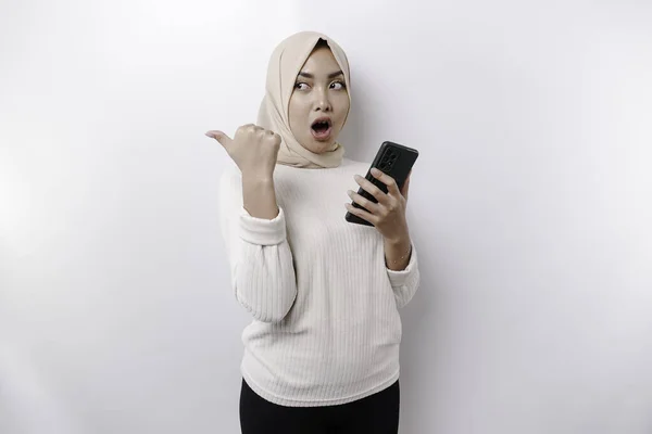 Zszokowana Azjatycka Muzułmanka Hidżabie Wskazująca Miejsce Przy Telefonie Odizolowana Białym — Zdjęcie stockowe