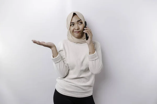 白い背景によって隔離された電話で話している間 ヒジャーブを身に着けている思慮深い若いアジアのイスラム教徒の女性と彼女の横にコピースペースを指す — ストック写真
