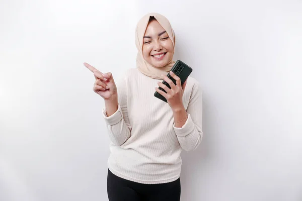 Возбужденная Азиатка Носящая Хиджаб Указывая Пространство Рядом Ней Держа Телефон — стоковое фото