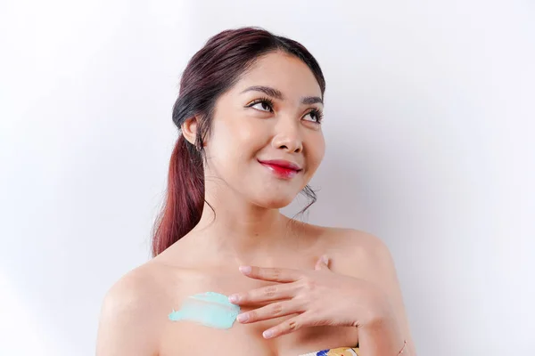 Skin Care Products Concept. Asian woman applying moisturizing lotion on body after shower, standing wrapped in towel, cropped image