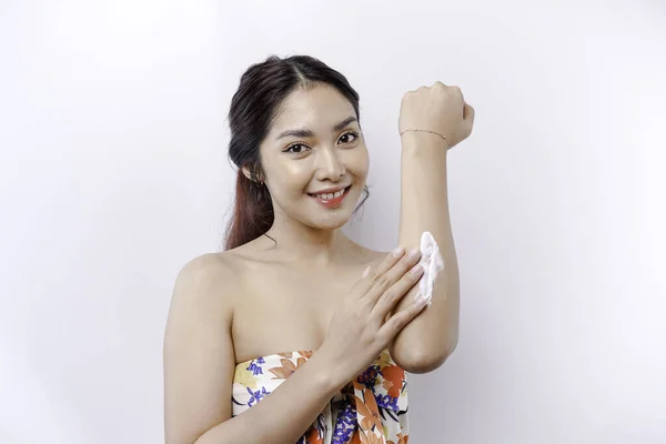 Skin Care Products Concept. Asian woman applying moisturizing lotion on body after shower, standing wrapped in towel, cropped image