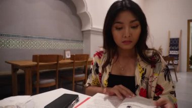 Restoranda oturmuş kitap okuyan sevimli bir Asyalı kadın.