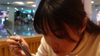 Çekici bir Asyalı kadın restoranda yemek yiyor, erişte yiyor ya da çubukla Japon eriştesi yiyor.