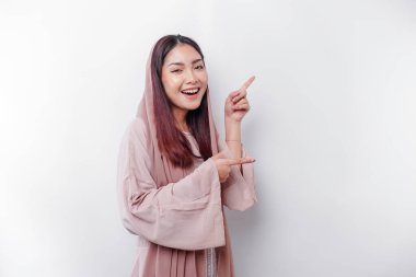 Young Asian Muslim woman smiling while pointing to copy space beside her