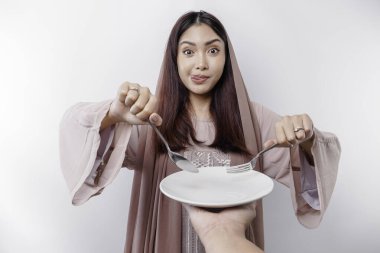 Gülümseyen Asyalı Müslüman bir kadın oruç tutuyor, aç ve bir tabağı işaret ediyor.
