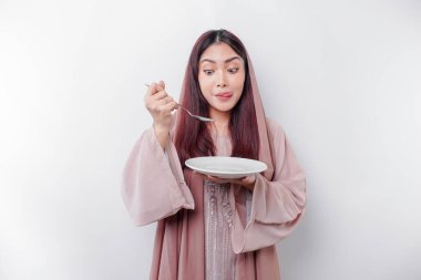 Gülümseyen Asyalı Müslüman bir kadın oruç tutuyor, aç ve bir tabağı işaret ediyor.