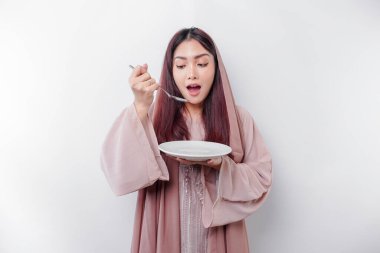 Gülümseyen Asyalı Müslüman bir kadın oruç tutuyor, aç ve bir tabağı işaret ediyor.