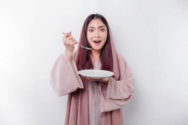 Gülümseyen Asyalı Müslüman bir kadın oruç tutuyor, aç ve bir tabağı işaret ediyor.