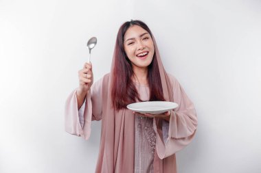 Gülümseyen Asyalı Müslüman bir kadın oruç tutuyor, aç ve bir tabağı işaret ediyor.